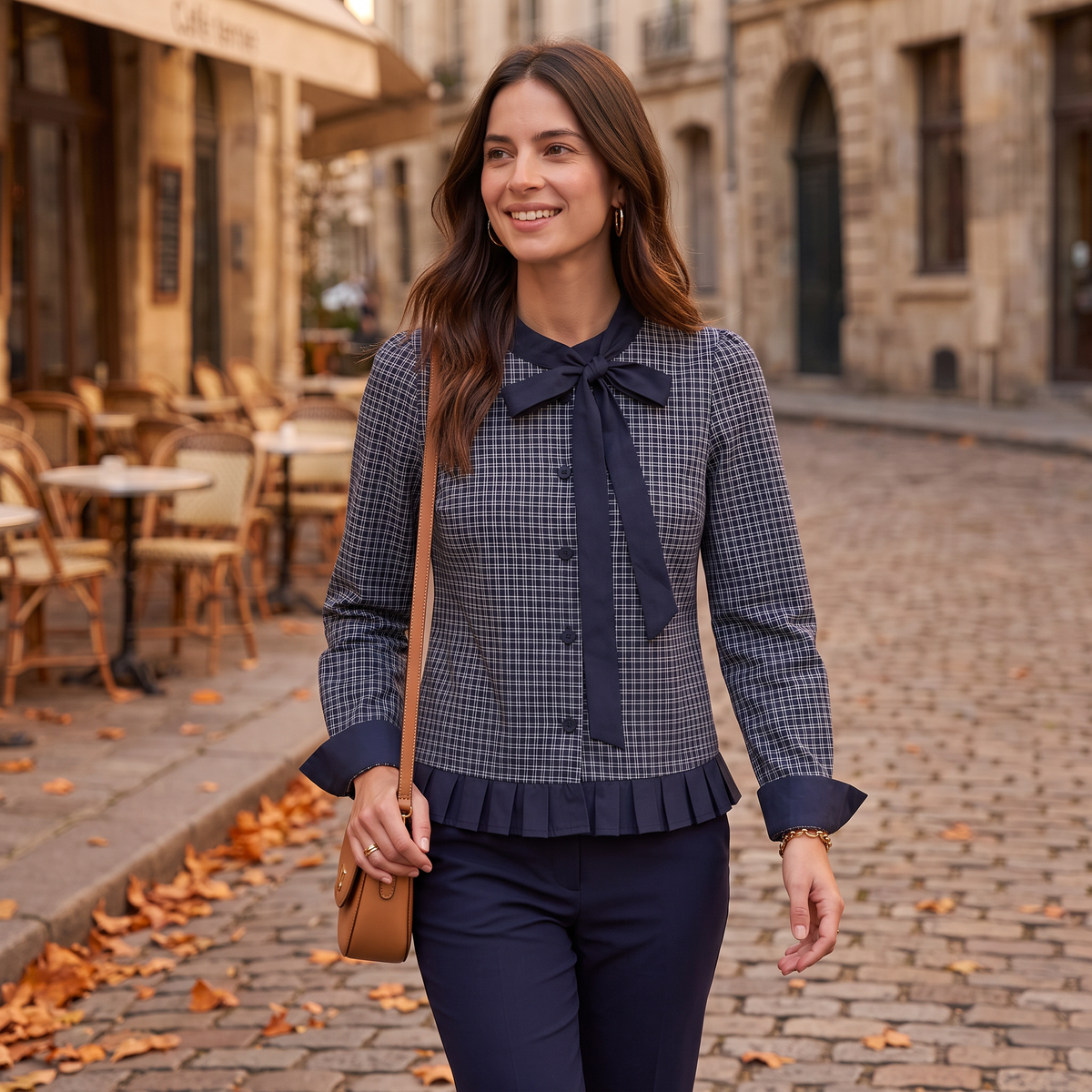 Mujer paseando por una calle empedrada en otoño con una blusa de cuadros con lazo al cuello