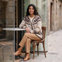 Mujer sentada en la terraza de un café con un cárdigan jacquard nórdico con capucha beige