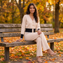 Mujer sentada en un banco de parque en otoño con conjunto punto cárdigan bicolor y pantalón ancho en color beige