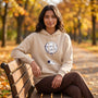 Essyro beige hoodie with a hand-drawn astronaut and moon graphic, worn by a woman sitting on a park bench in autumn.
