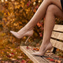 Essyro beige patent leather stiletto pumps with pointed toe worn by a woman sitting on a park bench in autumn