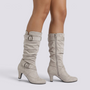 Essyro slouch boots in beige faux suede with mid-curved heels, decorative buckles, and side zipper closure.