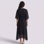 Back view of a woman wearing an Essyro black midi dress with batwing sleeves, cinched waist, and asymmetric hem.