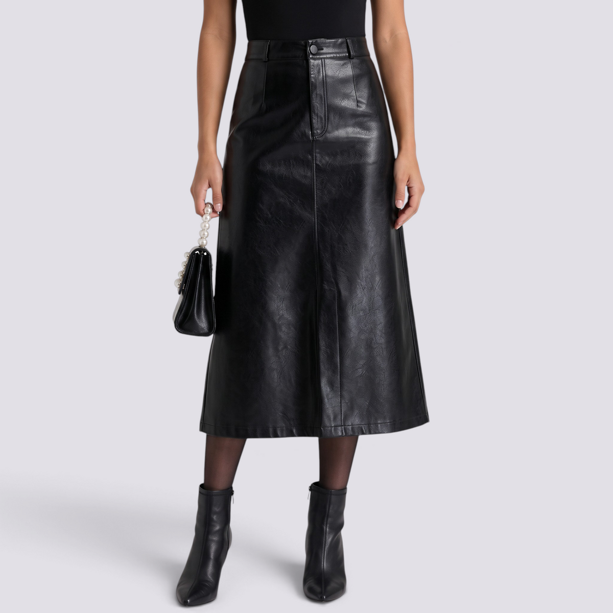 Essyro black faux leather midi skirt with high waist, front slit, and A-line silhouette worn with black ankle boots.