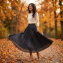 Essyro metallic pleated maxi skirt in black worn by a smiling woman in an autumn park with a white sweater and heels