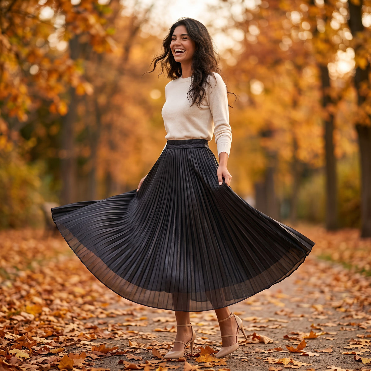 Essyro metallic pleated maxi skirt in black worn by a smiling woman in an autumn park with a white sweater and heels