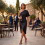 Essyro black one-shoulder satin party dress with asymmetrical hem worn by a woman holding a glass at an evening event