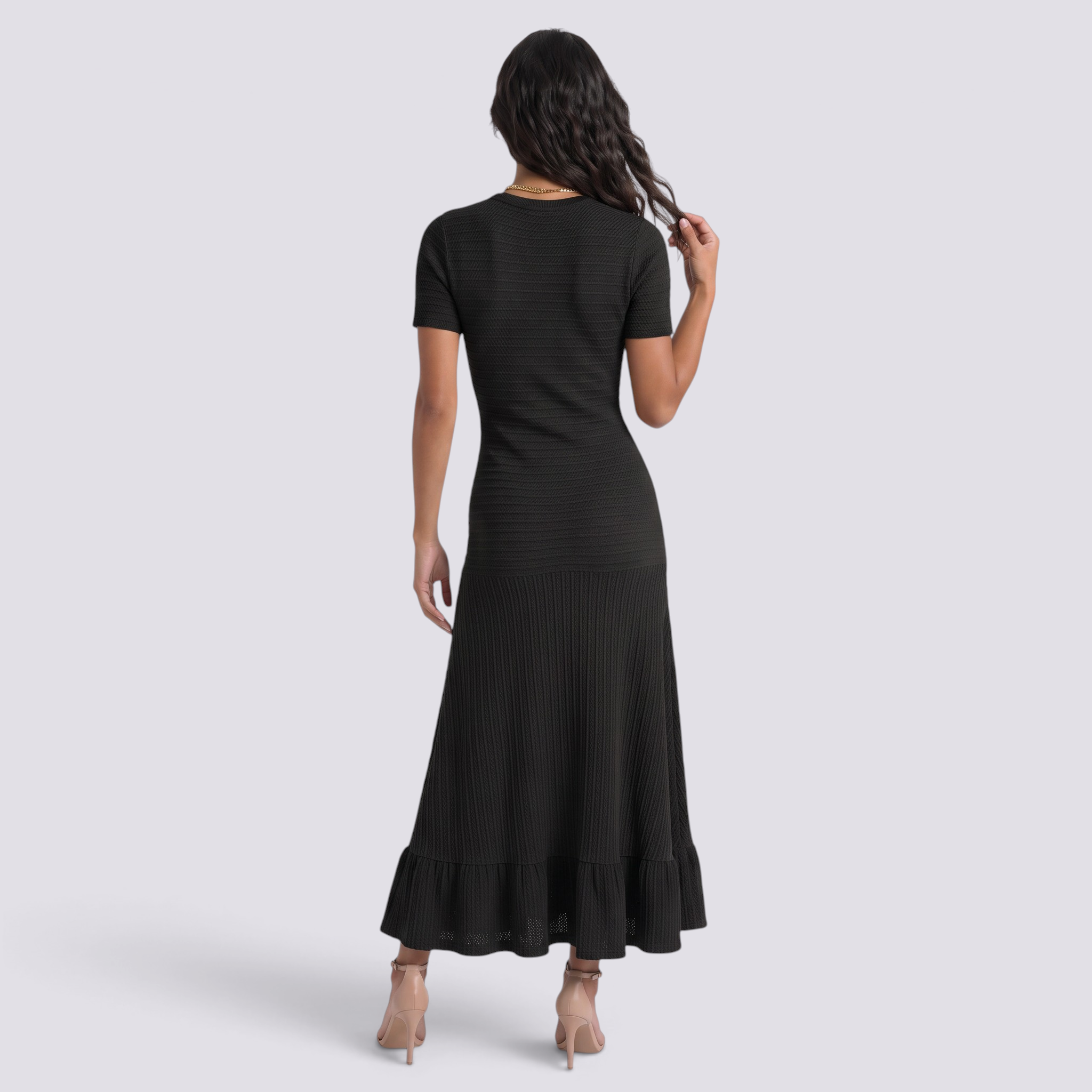 Back view of a woman wearing an Essyro black ribbed knit maxi dress with short sleeves and a ruffled hemline.