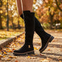 Essyro black suede knee-high boots with gold buckle detail and chunky track sole worn in an autumn park setting