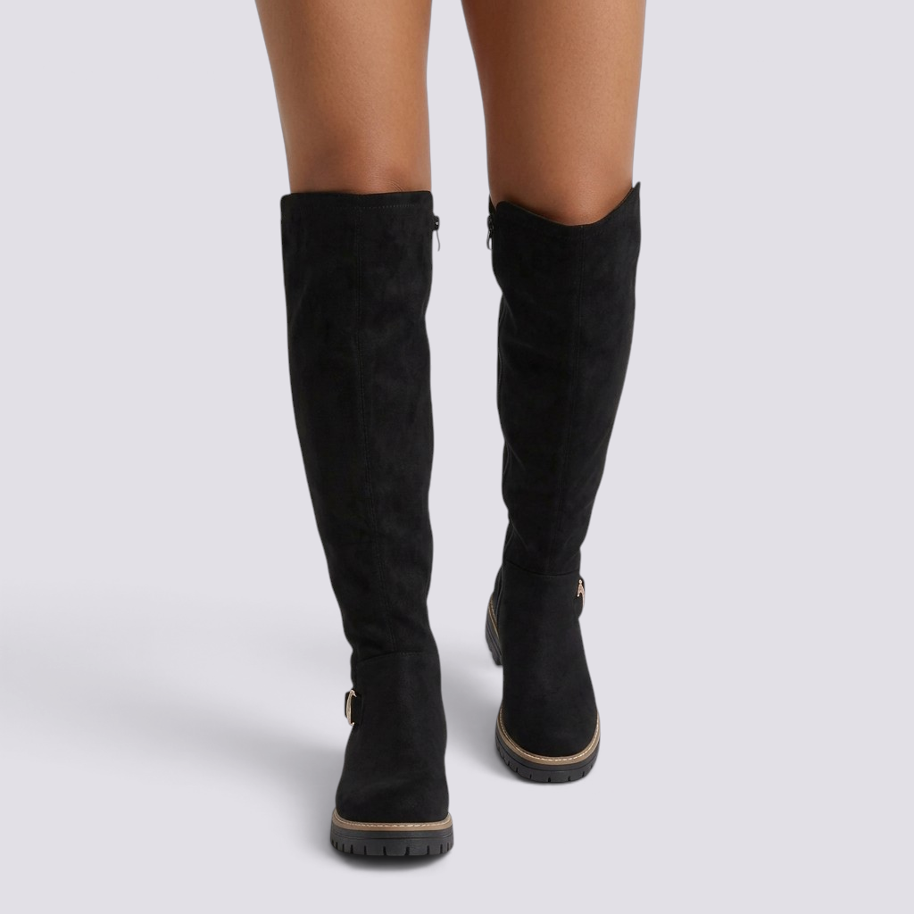 Essyro black knee-high suede boots with gold buckle detail and chunky track sole worn by a model