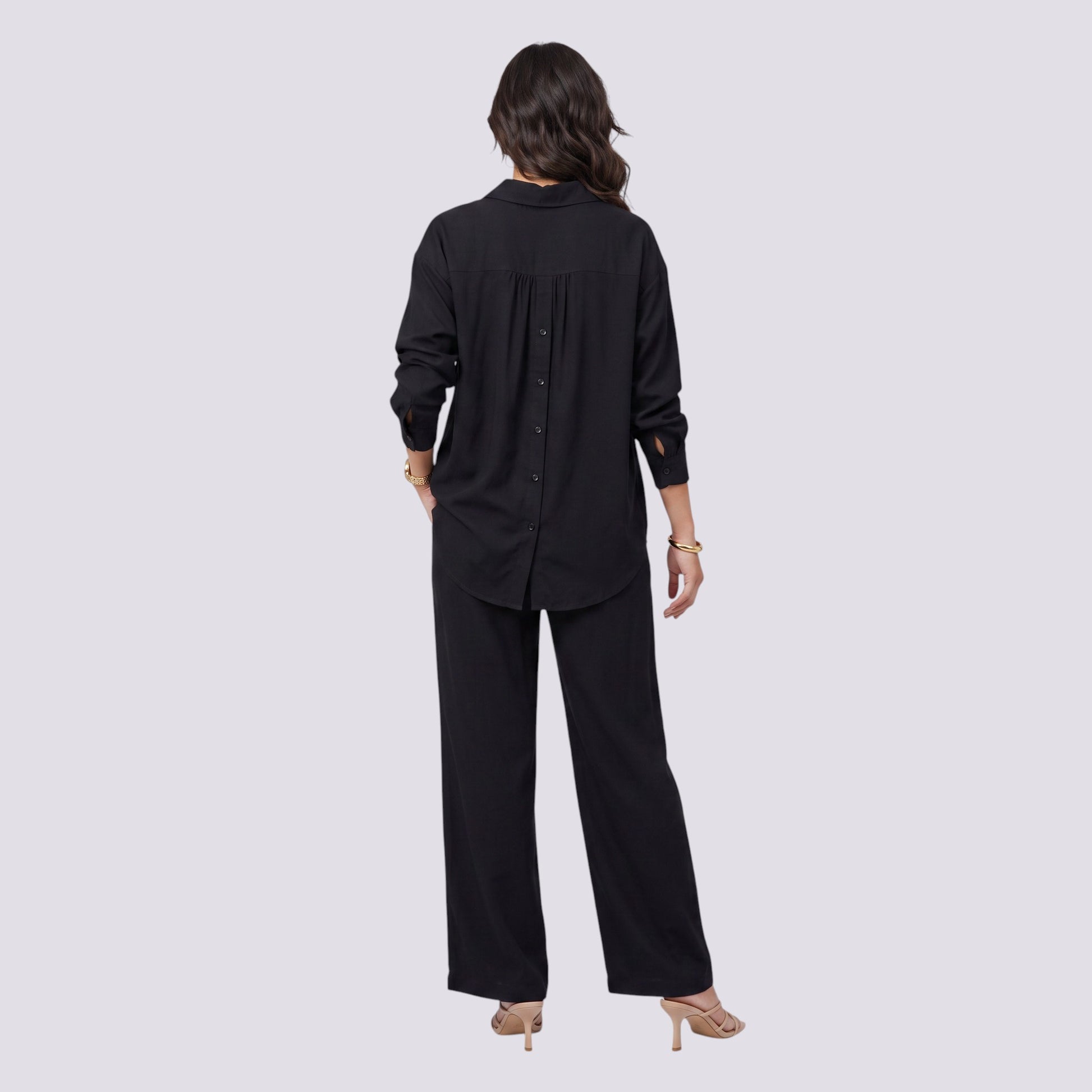 Back view of a woman wearing an Essyro black two-piece set featuring a button-back shirt and wide-leg trousers.