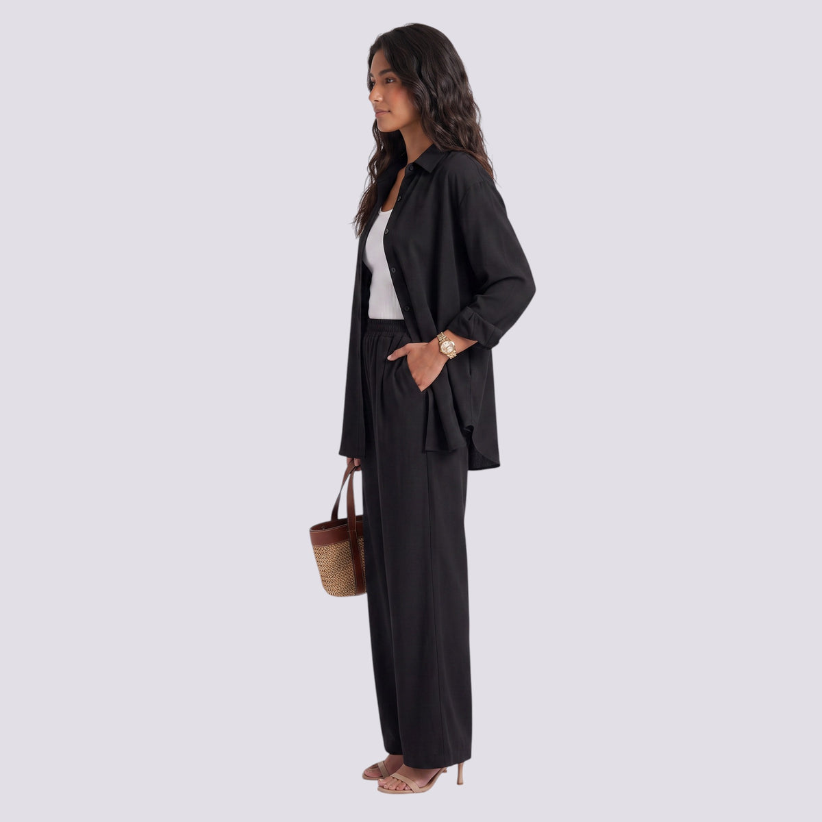 Essyro black two-piece set with long-sleeve loose shirt and wide-leg trousers worn by a woman with a straw handbag.