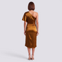 Back view of an Essyro one-shoulder bronze satin midi dress with an asymmetrical hem on a model wearing heels.