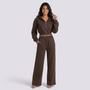 Essyro brown cropped zip-up hoodie and wide-leg trousers set worn by a smiling woman against a white background.