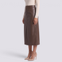 Essyro brown faux leather midi skirt with high waist, front slit, and side pockets worn with beige heels.