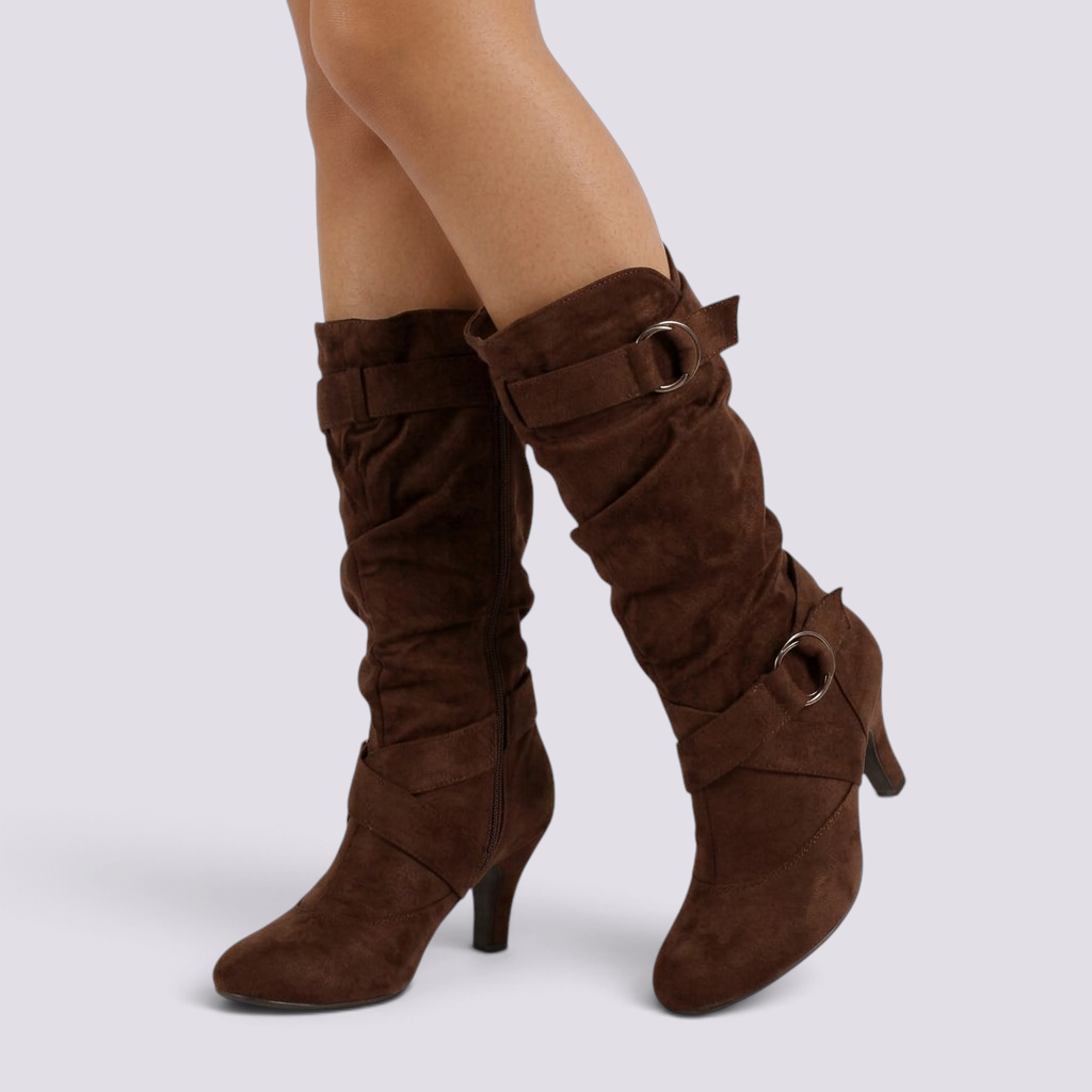 Essyro brown faux suede slouch boots with mid-curved heels and decorative side buckles on a woman's legs.