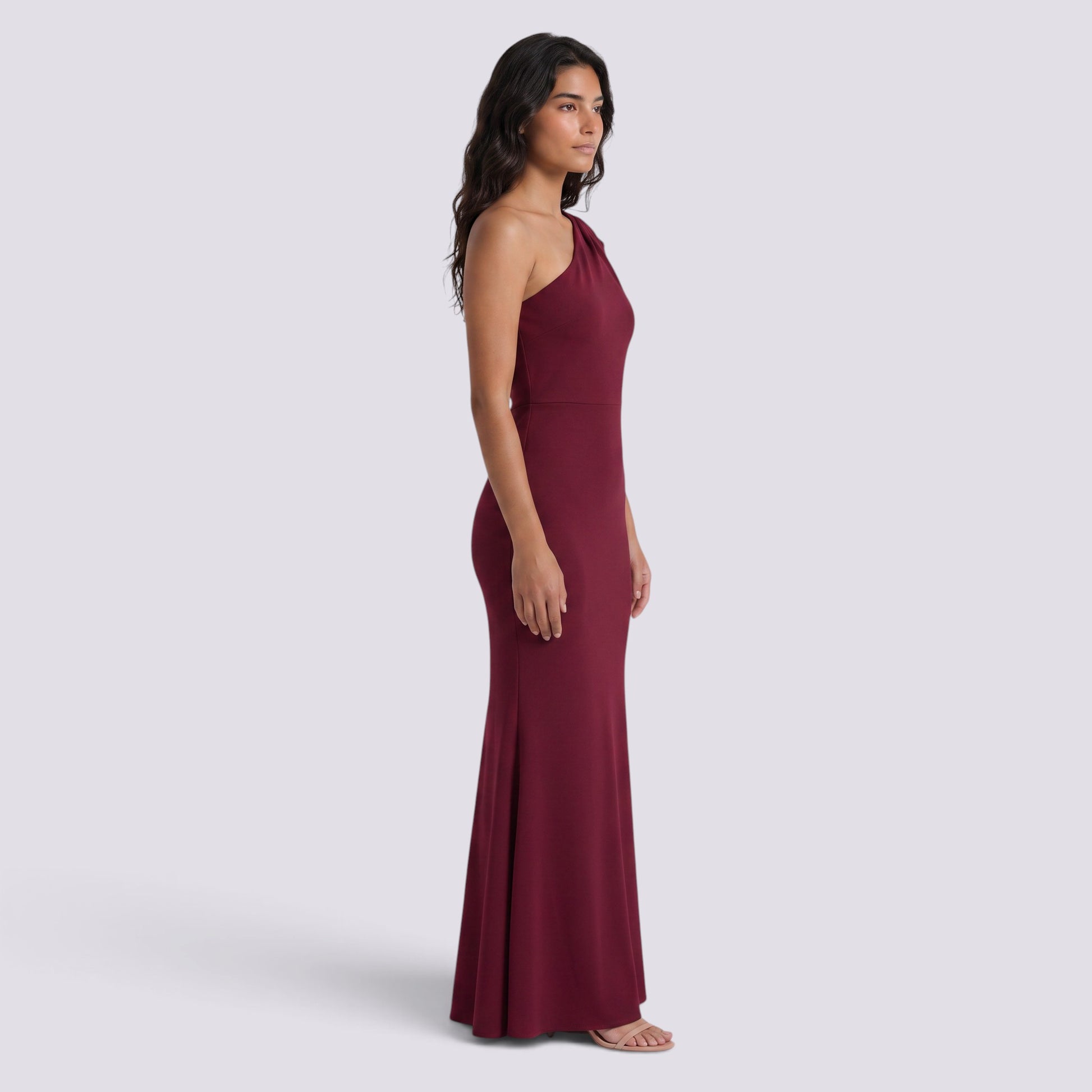 Essyro burgundy floor-length mermaid gown with an asymmetric one-shoulder neckline and draped sleeve detail.