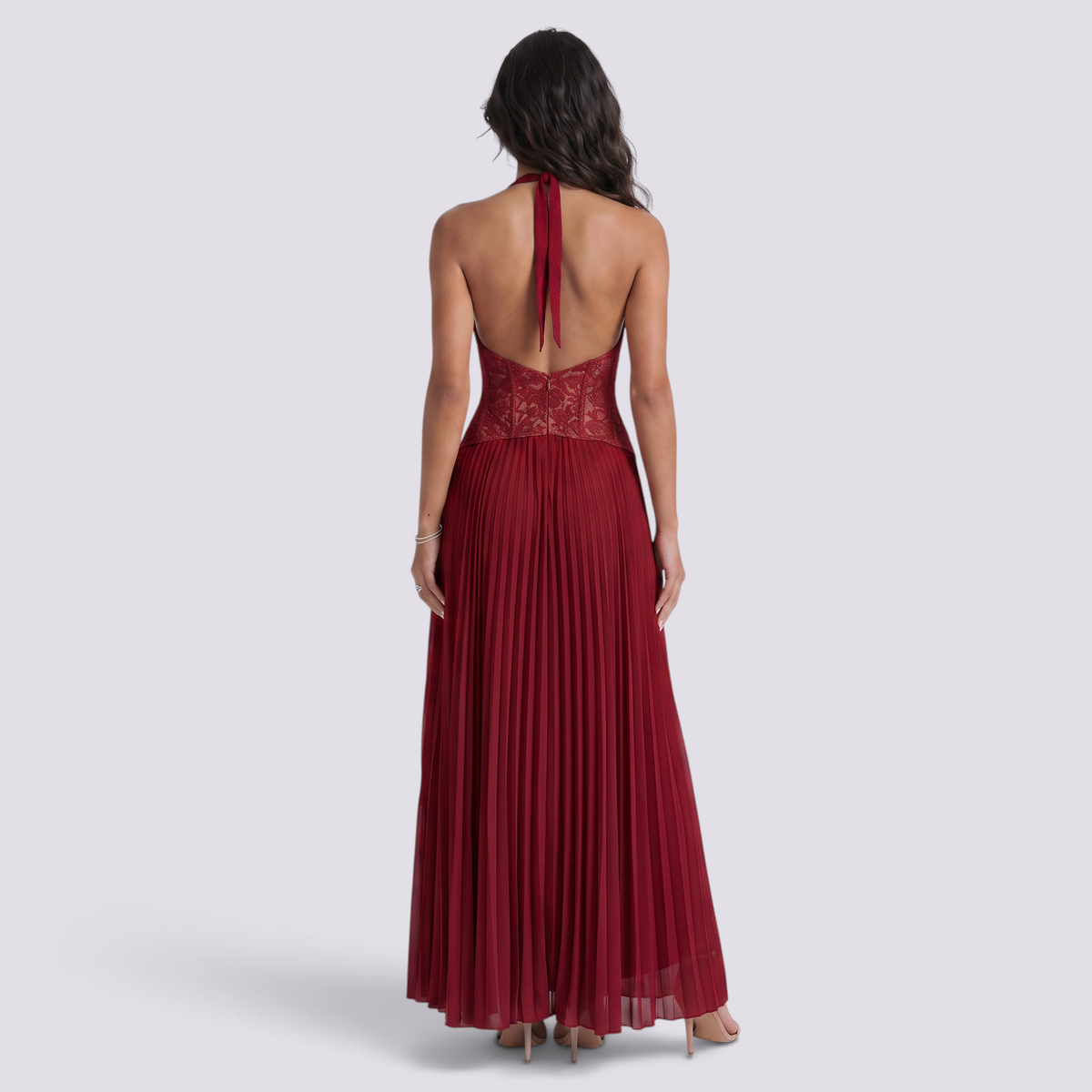 Essyro back view of a burgundy floor-length pleated gown with a corset bodice and open back halter neckline.