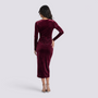 Back view of a woman wearing an Essyro burgundy velvet midi dress with long sleeves and a fitted silhouette.