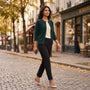 Essyro dark green wool cardigan with round neck and button closure worn by a woman walking on a cobblestone street