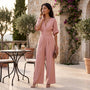 Essyro dusty pink palazzo jumpsuit with V-neck, wide waist belt, and three-quarter sleeves on a Mediterranean terrace.