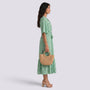 Essyro bohemian green patterned maxi dress with V-neck and short sleeves worn by a model holding a straw bag