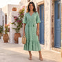 Essyro green boho maxi dress with V-neck, short sleeves, and geometric pattern worn by a woman in a sunny village.