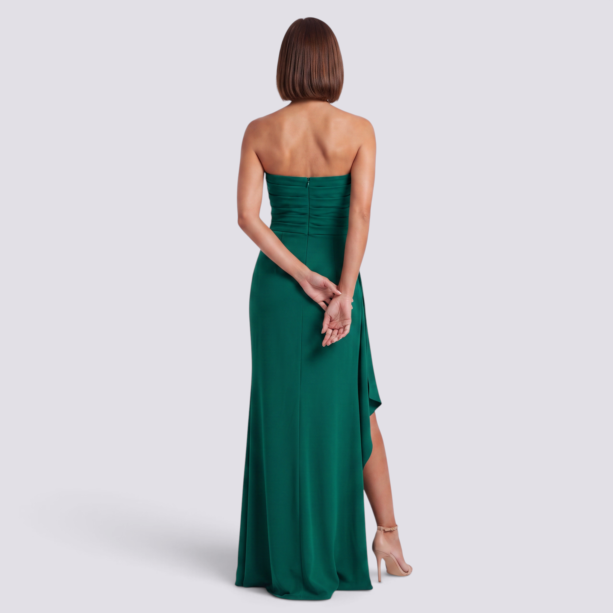 Essyro emerald green strapless maxi dress with side slit and pleated skirt worn by a woman from the back view