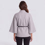 Back view of Essyro short grey cape with high collar, batwing sleeves, and a thin black belt, worn over black pants.