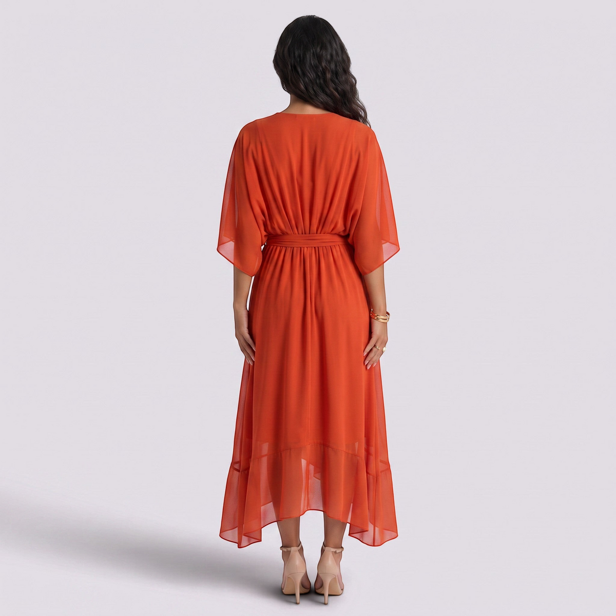 Essyro long orange dress with batwing sleeves, cinched waist, and asymmetrical hem worn by a woman from behind.
