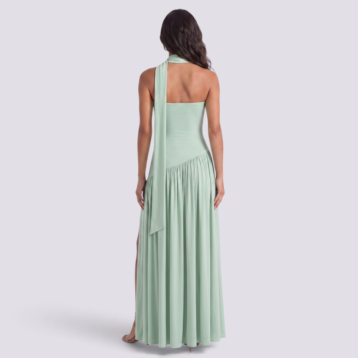 Back view of a woman wearing an Essyro mint green floor-length halter dress with an asymmetrical draped skirt.