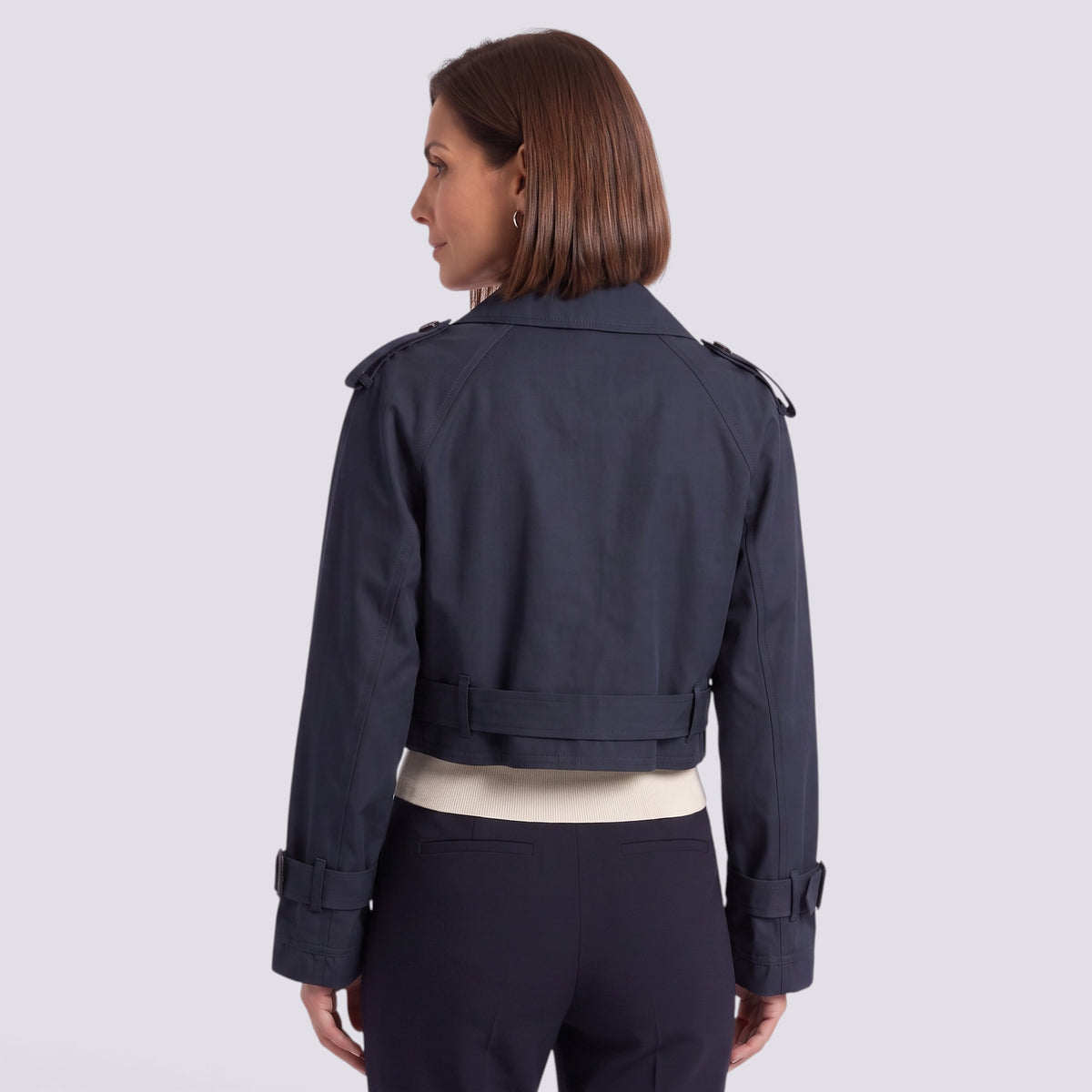 Essyro navy blue cropped windbreaker jacket with long sleeves and belted waist detail, worn by a woman from behind.