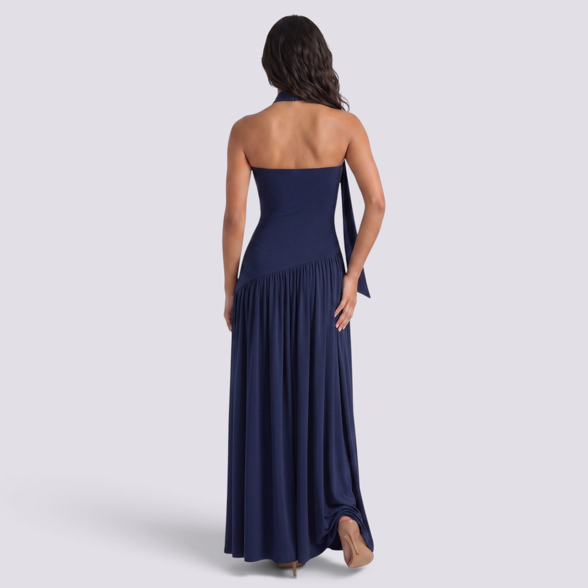 Back view of a woman wearing an Essyro navy blue halter neck maxi dress with an asymmetrical draped skirt
