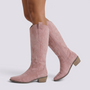Essyro pink suede knee-high western boots with delicate embroidery and a pointed toe worn by a model.