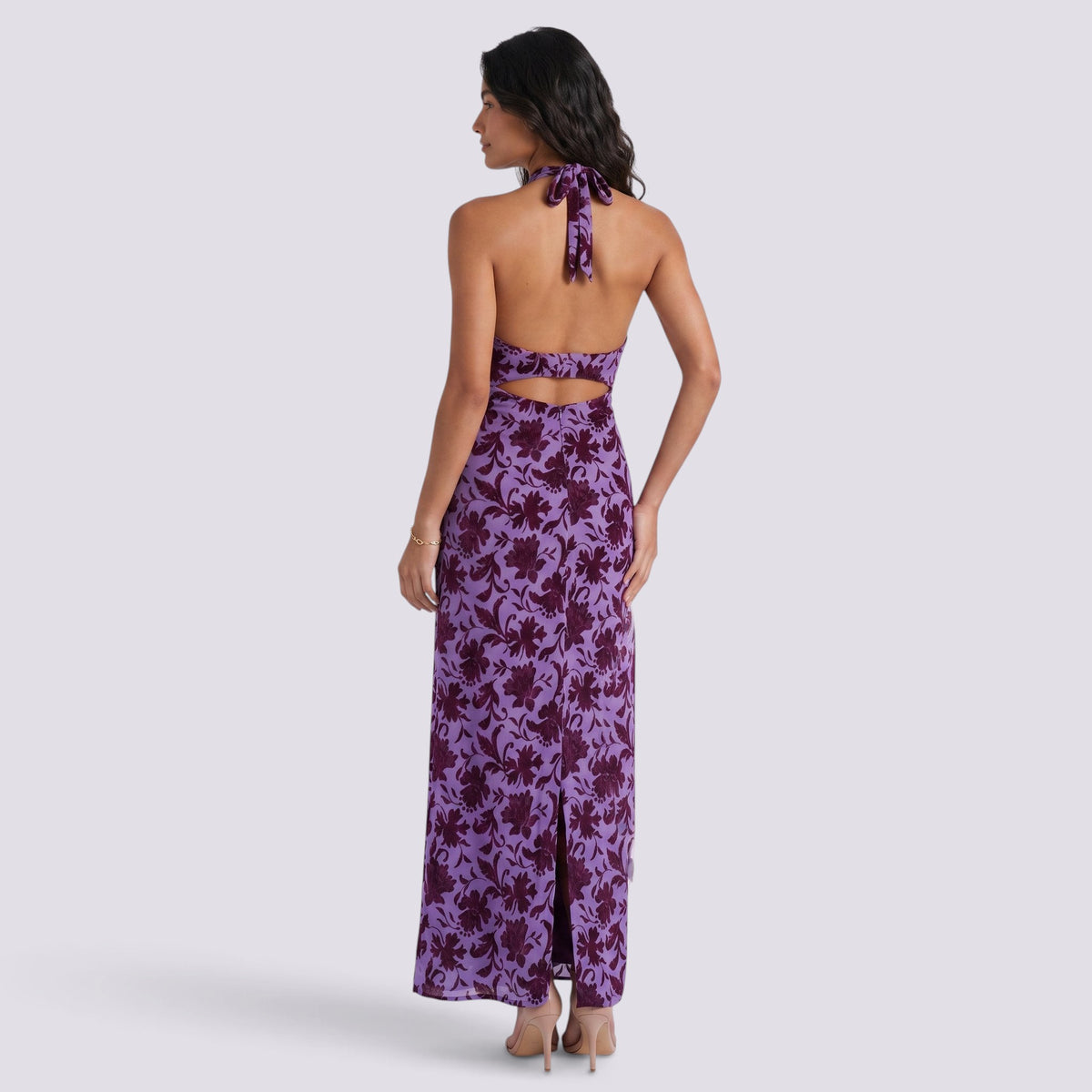 Essyro purple floral maxi dress with halter neck, open back, and side slit worn by a model, back view.