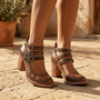 Essyro brown snake-effect leather block heel shoes with triple ankle buckles and round toe on a stone patio.