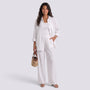 Essyro white two-piece set with a loose long-sleeve shirt and wide-leg trousers worn by a woman holding a straw bag.