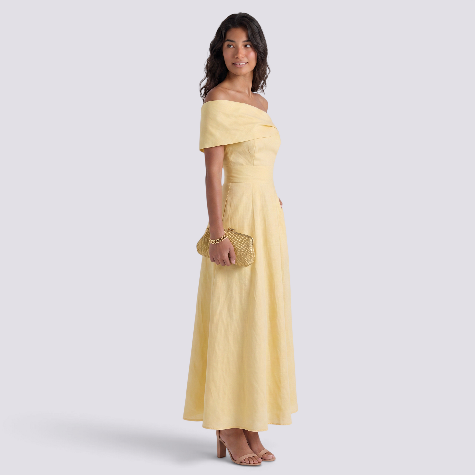 Essyro elegant pale yellow off-the-shoulder maxi dress with a fluid silhouette worn by a model with a gold clutch