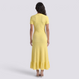 Back view of a woman wearing an Essyro yellow ribbed knit maxi dress with short sleeves and a ruffled hemline.