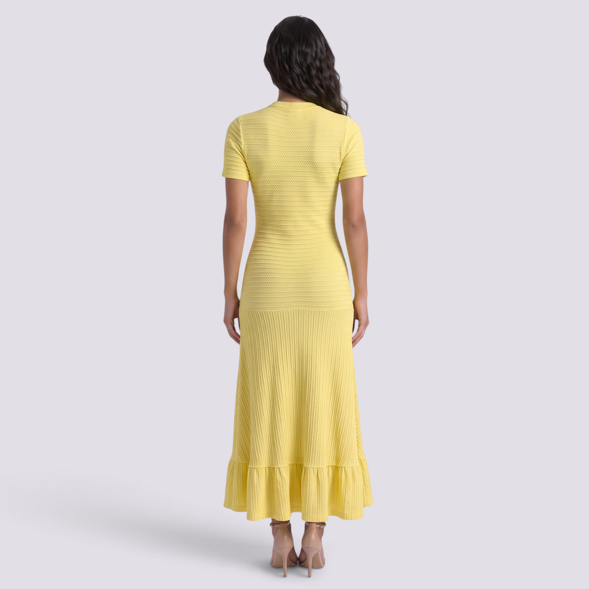 Back view of a woman wearing an Essyro yellow ribbed knit maxi dress with short sleeves and a ruffled hemline.