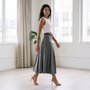 Mujer caminando por un loft luminoso con falda midi plisada gris de cintura alta y top blanco