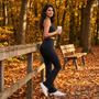 Mujer con leggings acampanados negros con bolsillos apoyada en una valla de madera en un parque de otoño