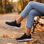 Zapatillas deportivas mujer de malla negras con cuña baja, sentada en un banco del parque en otoño