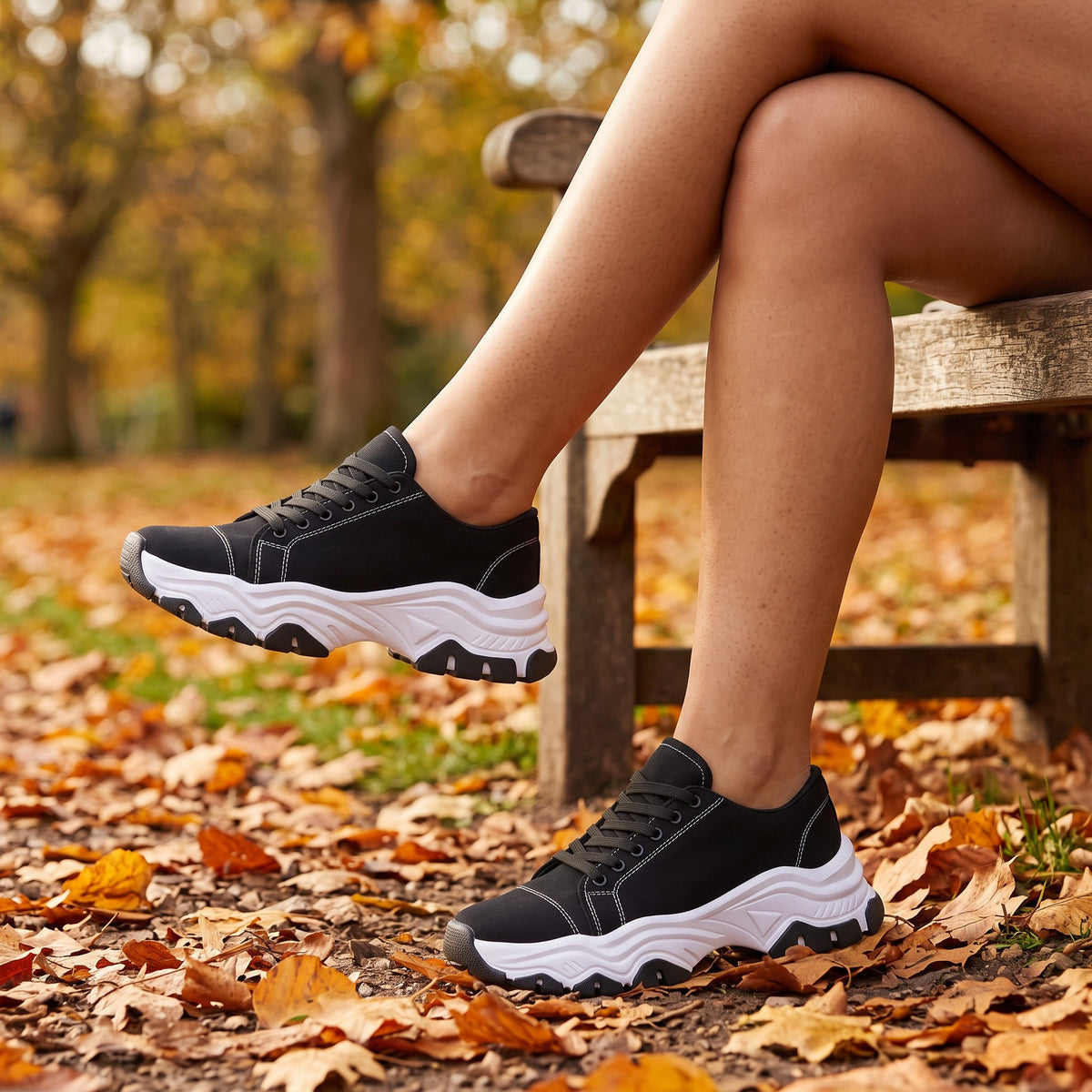 Mujer sentada en un banco de parque en otoño con zapatillas deportivas negras de suela ondulada y cordones