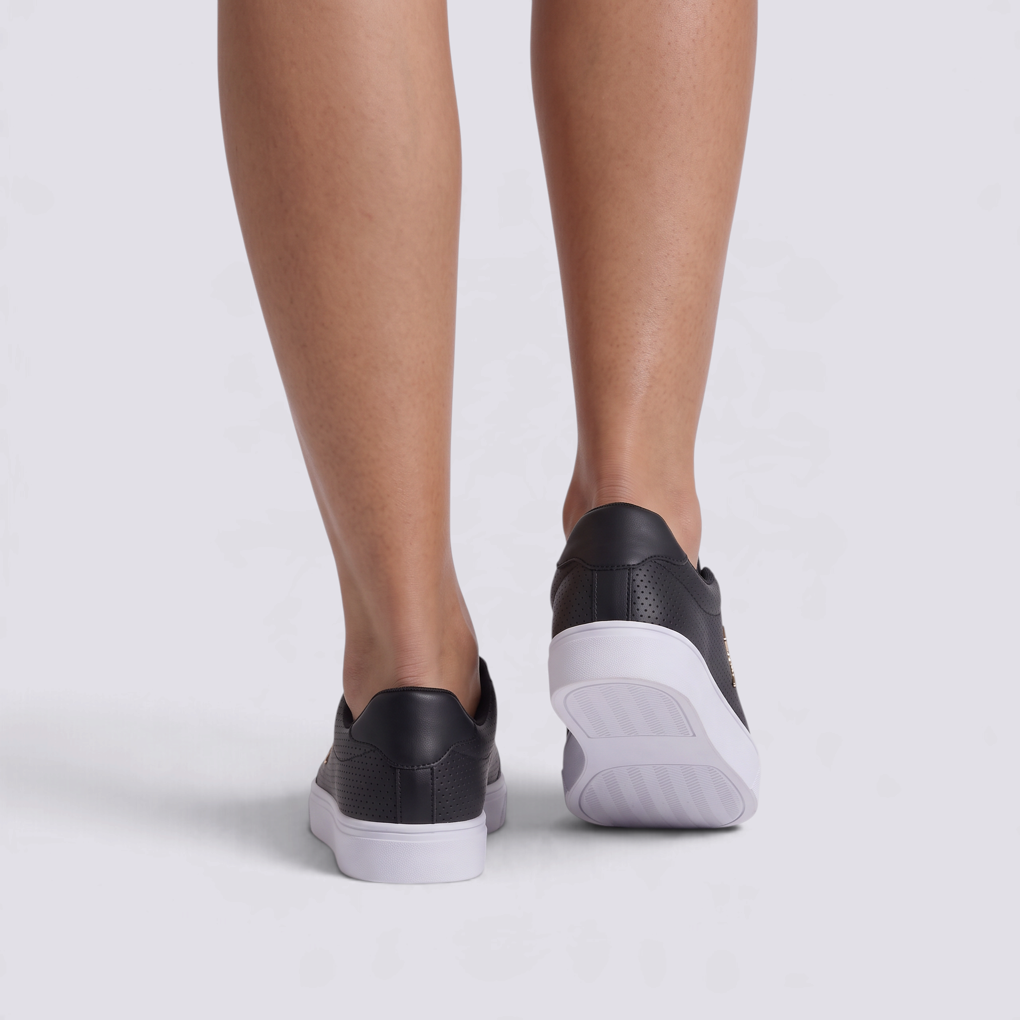 Zapatillas planas perforadas con detalle dorado en negro, vista trasera