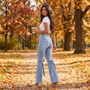 Mujer paseando por un parque en otoño con vaqueros acampanados de tiro alto y lazos en color azul claro