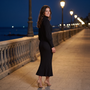 Vestido largo de mujer de punto acanalado con cuello alto, manga farol y bajo sirena color negro, look nocturno en paseo marítimo con farolas