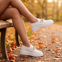 Mujer sentada en un banco de parque en otoño con zapatillas slip-on blancas con cadena dorada